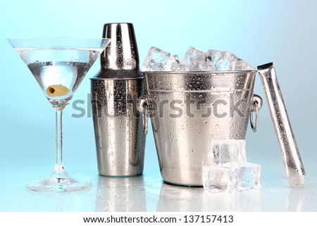 Metal ice bucket and shaker and cocktail on blue background