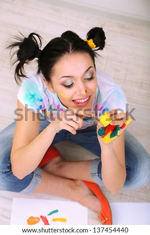 Young pretty painter with hands in paint, on gray background
