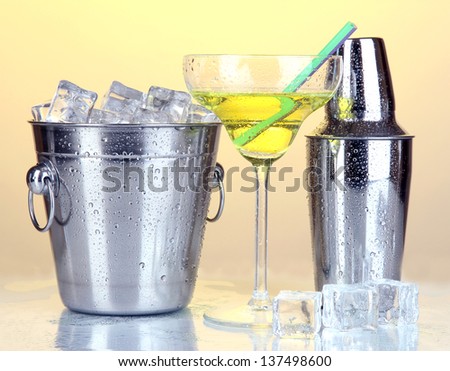 Metal ice bucket and shaker and cocktail on yellow background