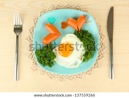 Sausages in form of hearts, scrambled eggs and parsley, on color plate, on wooden background
