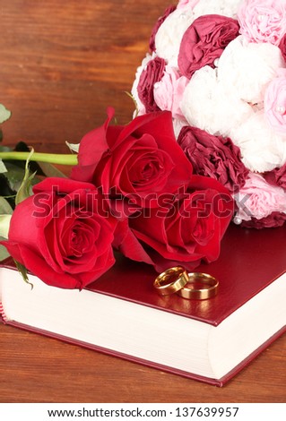 Wedding rings on bible with roses on wooden background