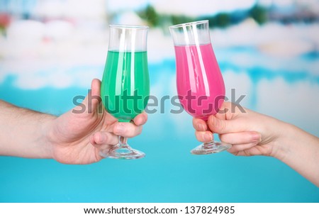 Cocktails in men\'s and women\'s hands on pool background