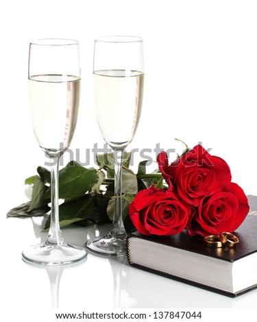 Wedding rings on bible with roses and glasses of champagne isolated on white