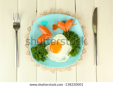 Sausages in form of hearts, scrambled eggs and parsley, on color plate, on wooden background