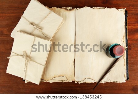 Open old book, letters and ink pen on wooden background
