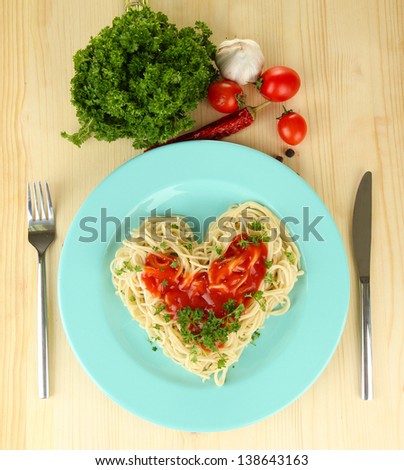 Cooked spaghetti carefully arranged in  heart shape and topped with tomato sauce, on  wooden background