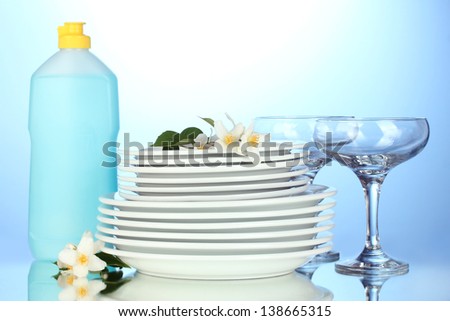 empty clean plates and glasses with dishwashing liquid on blue background
