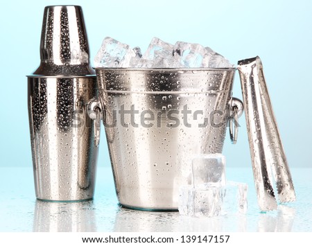 Metal ice bucket and shaker on blue background