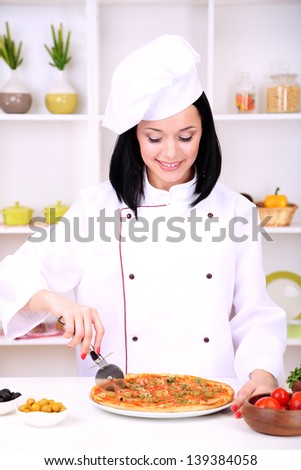 Beautiful girl chief-cooker with pizza on kitchen background