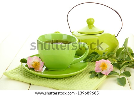 Cup and teapot of herbal tea with hip rose flowers on white wooden table
