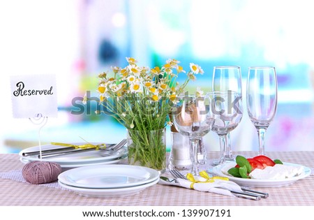 Table setting with chamomiles on checkered tablecloth on window background