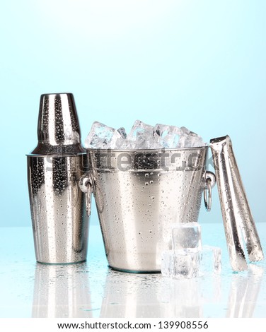Metal ice bucket and shaker on blue background
