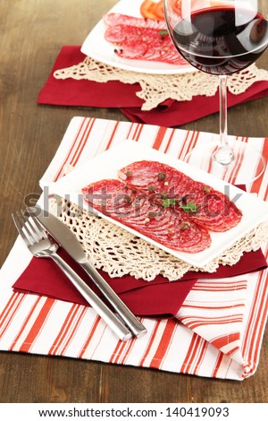 Tasty salami on plates on wooden table close-up