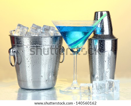Metal ice bucket and shaker and cocktail on yellow background