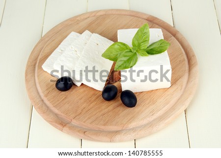 Sheep milk cheese, black olives, with basil on cutting board, isolated on white
