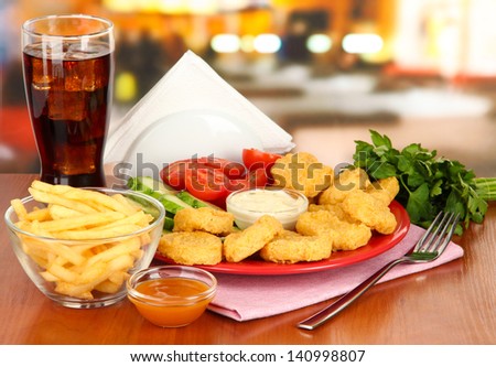 Fried chicken nuggets with vegetables,cola,french fries and sauce on table in cafe