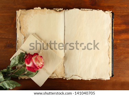 Open old book, letters and rose on wooden background