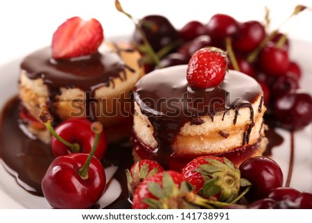 Tasty biscuit cakes with chocolate and berries on plate, close up
