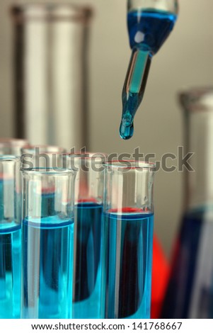 Laboratory pipette with drop of color liquid over glass test tubes, close up