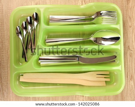 Green plastic cutlery tray with checked cutlery on wooden table