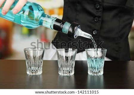 Barmen hand with bottle  pouring beverage into glasses, on bright background