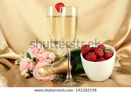Romantic still life with champagne, strawberry and pink roses, on color fabric background