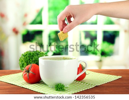 Cup of soup with bouillon cube on wooden table