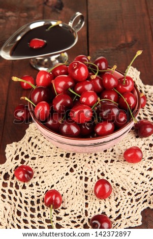Ripe red cherry berries in bowl and chocolate sauce on wooden table close-up