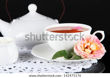 Kettle and cup of tea from tea rose on napkin black background