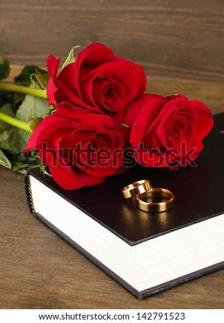 Wedding rings on bible with roses on wooden background