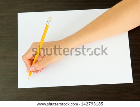 Hand with pencil on white paper, on wooden background