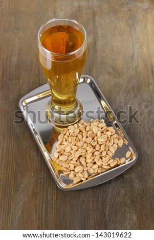 Beer in glass and nuts on tray on wooden table