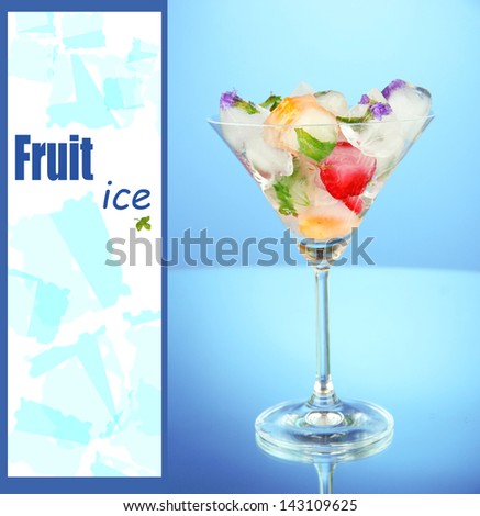 Ice cubes with flowers and herbs and fruits inside in martini glass, on blue background