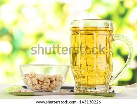 Beer in glass and nuts on tray on wooden table on nature background