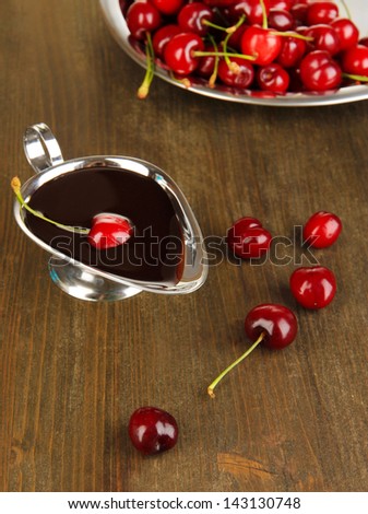 Ripe red cherry berries in plate and chocolate sauce on wooden table close-up