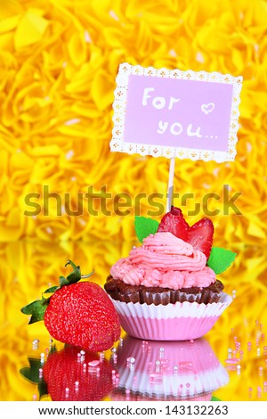 Beautiful strawberry cupcake with postcard on decorative yellow background