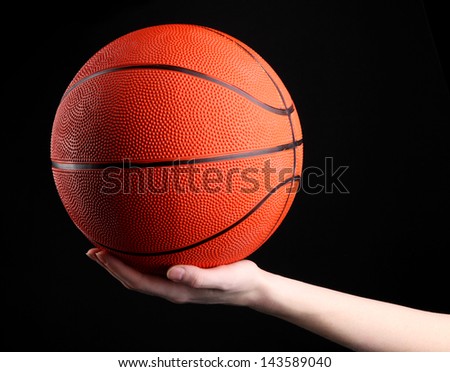 Basketball in woman hand on black background
