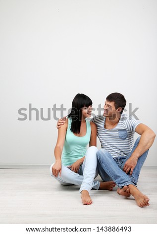 Beautiful loving couple sitting on floor in room on grey background