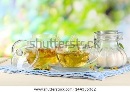 Kettle and cup of tea with linden on napkin on wooden table on nature background