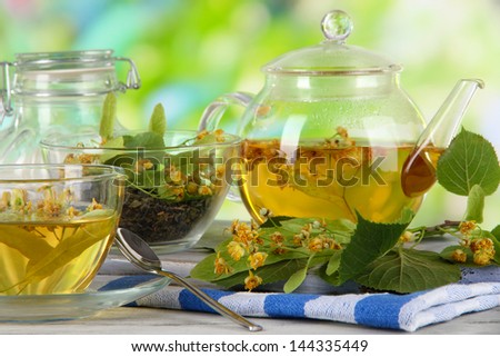 Kettle and cup of tea with linden on  wooden table on nature background