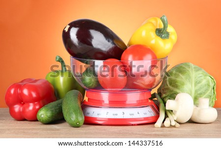 Fresh vegetables in scales on table on orange background