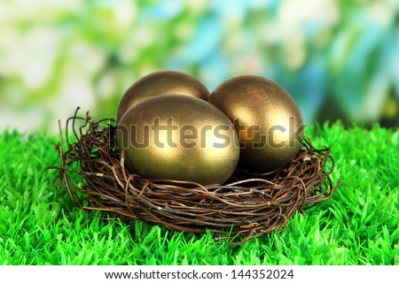 Three golden eggs in nest on grass on bright background