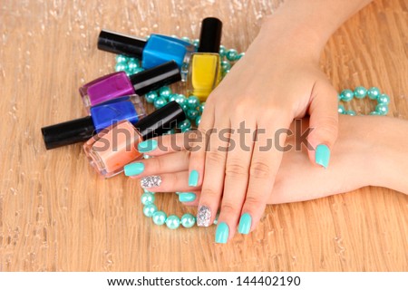 Beautiful woman hands with blue manicure holding beads and bottles with nail polish, on color background