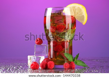 Iced tea with raspberries and mint on purple background