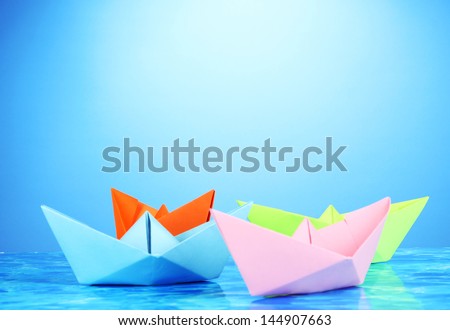 Paper ships of different colors on water background