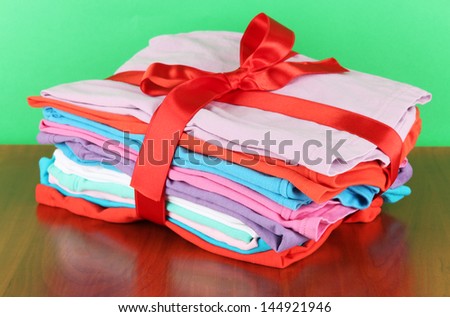 Pile of clothing with red ribbon and bow on table on green background