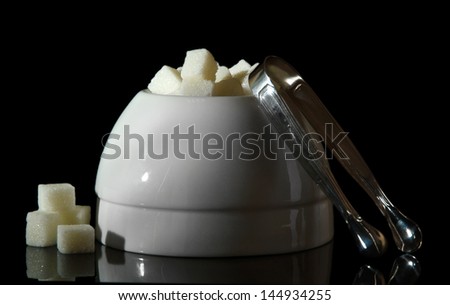 Refined sugar in white sugar bowl on black background
