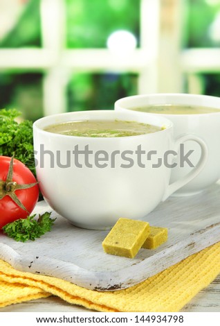 Cups of soup with bouillon cubes on wooden table