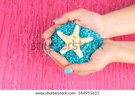 Beautiful woman\'s hands holding handful of sea salt, on color background