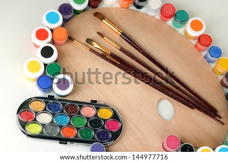 Wooden art palette with brushes for painting and paints isolated on white